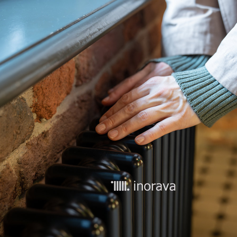 Woman warming hands near old vintage radiator at home, checking heating system working capacity